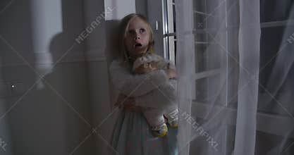 Close-up of scared Caucasian blond girl hugging doll and yelling. Portrait of frightened child standing next to the big