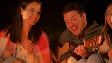 Friends roasting marshmallow and playing guitar