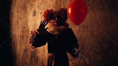 Scary clown with colorful makeup in a carnival costume, looking into the camera