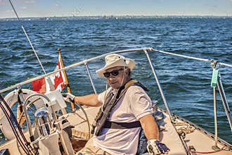 An elderly seafarer manages a sailing boat on a sunny summer day.