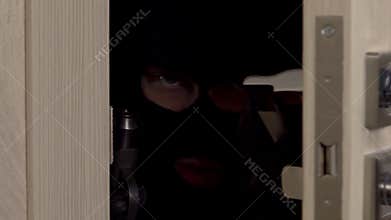 Burglar behind the door with a gun closeup. The masked thug slowly opened the door and went into the room.