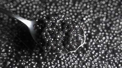 Spoon with black caviar on a background of rotating black caviar