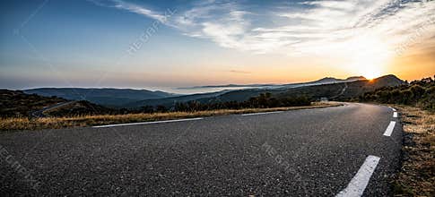 Empty long mountain road to the horizon on a sunny summer day at bright sunset