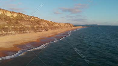 An aerial backward footage of the Hengistbury Head cliff with beautiful sandy beach and crystal blue water under a majestic blue s