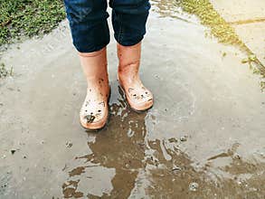 Closeup of girl child pink rain boots in muddy puddle. Seasonal spring summer fall kids activity outdoors. Child having fun