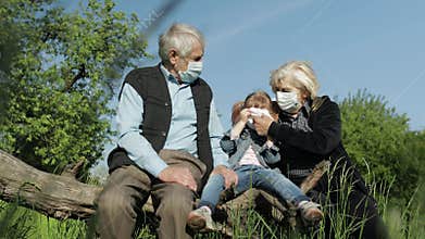 Grandparents with granddaughter in medical masks in park. quarantine