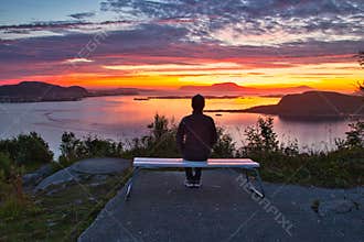 A Lone Man Sitting on A Bench Overlooking Islands and Ocean at Dramatic Sunset