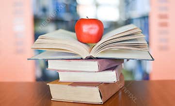 An apple on the books on the table with bookshelf in the library bookshelves background - Education learning concept open book
