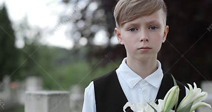 Close up view of sad kid raising head and looking to camera. Crop view of teen boy holding white lily flower while