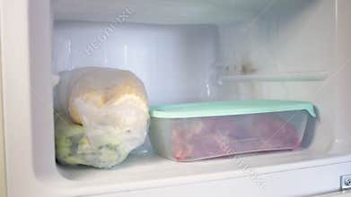 A man puts plastic containers in the fridge. Frozen fruits, vegetables, meat in the freezer.