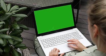 Woman using laptop computer on a outdoor terrace, blank green screen mockup copy space