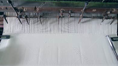 White fabric is getting sewn in the garment factory. Textile factory equipment.