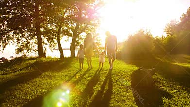 Happy family walking near the sea. Field and trees in countryside. Warm colors of sunset or sunrise. Loving parents and