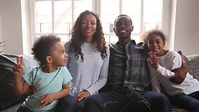 African family sitting on couch waving hands looking at camera