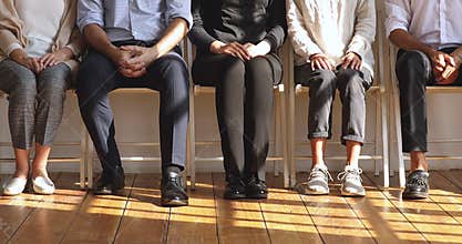 Professional unemployed business people sit on chairs, legs closeup view