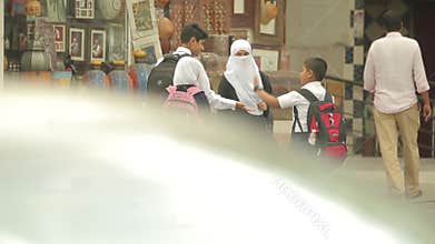 Omani schoolchildren greet each other on a city street, cars passing by.
