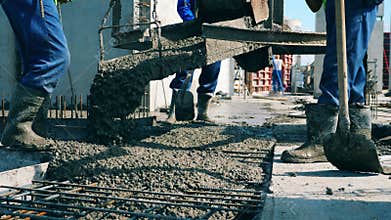 Male builders pour wet concrete on a floor while working on a construction site.