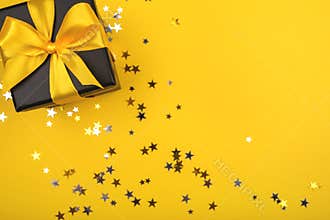 Gift box on yellow background with sparkling confetti