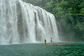 Tropical waterfall with boys on raft.
