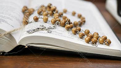 Phone charging from power bank and open holy bible with beads and cross on brown wooden table
