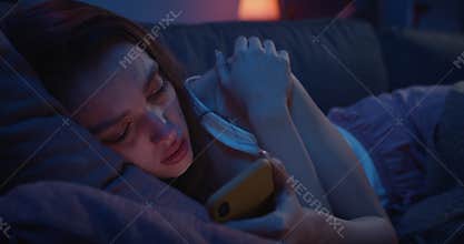 Close up of lonely young woman lying on sofa and using smartphone at night. Depressed millennial female starring at