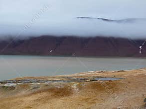 Panoramic view of arctic desert landscape and arctic ocean. Cloudy sky and mountains in the background. Svalbard, Norway