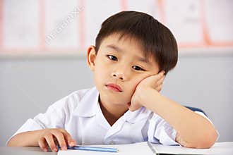 Unhappy Male Student Working At Desk In School