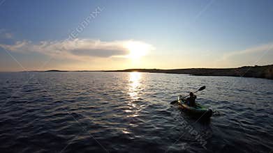 AERIAL: Kayaker woman kayaking on a calm sea towards sunset sky