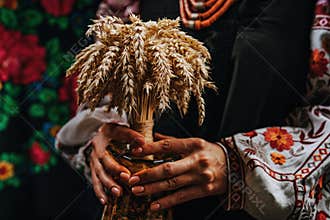 Ukrainian woman in authentic costume with Didukh on colorful ornaments carpet.