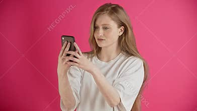 A ginger girl looks at her phone in surprise and laughs. Reads an e-book or messages from a friend. A young pretty woman