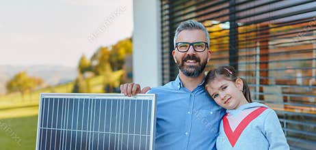 Father with his little daughter near their house with solar panels. Alternative energy, saving resources and sustainable