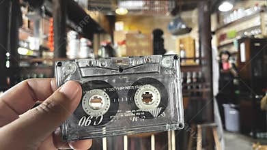 90s vibe, hand holding cassette tape with blurred background.