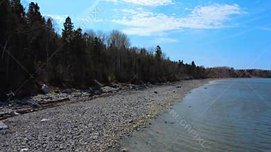 Flying over a rocky beach on the shore of a saltwater bay, rising above the surrounding forest.