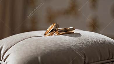 Golden wedding rings resting on soft cushion