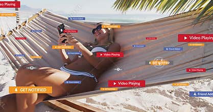 Woman reclining in hammock on beach, gently tapping smartphone and activating social media alerts
