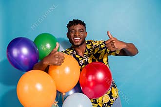 Joyful young man holding colorful balloons with thumbs up against a vibrant blue background