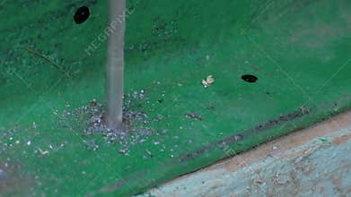 Drill bit boring through green painted metal angle bar