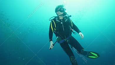 Diver holds action camera swimming near fish school