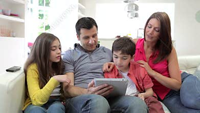 Hispanic Family Sitting On Sofa With Digital Tablet