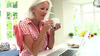 Middle Aged Woman Using Laptop And Eating Breakfast