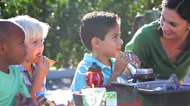 Children Eating Packed Lunch Outdoors With Teacher