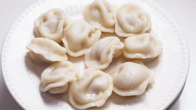 Boiled dumplings with dill are arranged in a circle on a white plate.