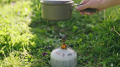 Person ignites portable gas stove with lighter, puts pot on. Outdoor scene features lightweight backpacking gear. For