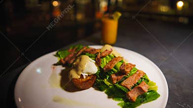 Gourmet steak on lettuce with sauce on a white plate, blurred bar background