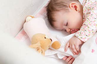 Baby girl sleeping in a cot with pacifier and toy