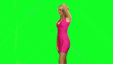 Attractive Caucasian blond woman wearing a pink dress, dancing, on fluorescent green background