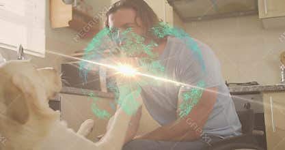 Holding raised paw, wheelchair user in light blue tee leaning in kitchen with dog, hologram globe