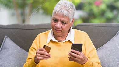 Happy senior woman making secure online purchases with credit card and smartphone at home