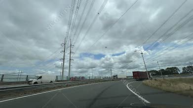 Highway curve with trucks vans and overhead powerlines under cloudy sky near