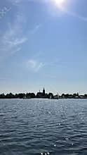 Sunny waterside panorama with sparkling lake, distant church silhouette
